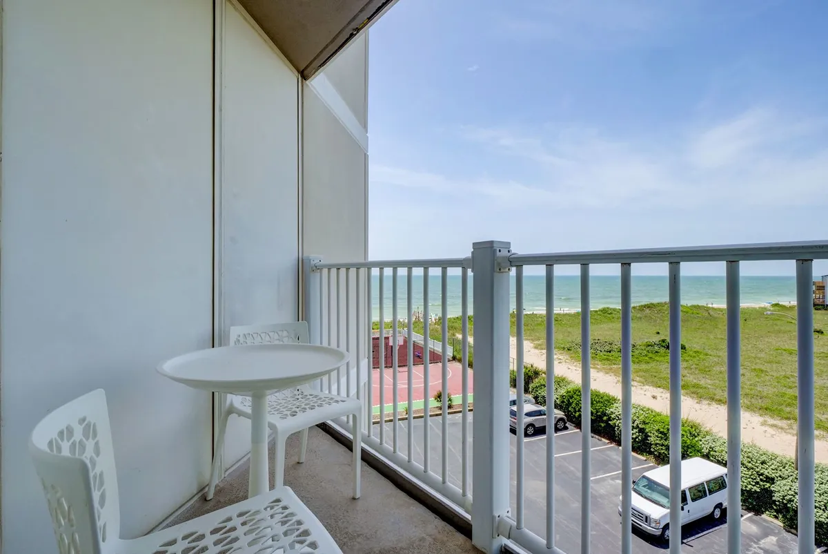 A serene private balcony with comfortable seating overlooking a tranquil ocean view and green landscape. The space is perfect for unwinding with a book, soaking in a sunrise, or letting the ocean breeze flow through the living space.