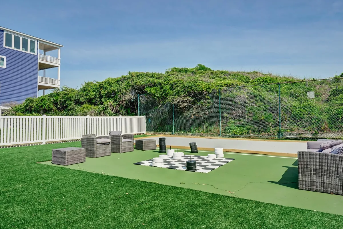 A playful outdoor chessboard set amid lush green grass, with comfortable lounge seating nearby. The scene is ideal for socializing, enjoying fresh air, and taking in sunset views after a productive day.