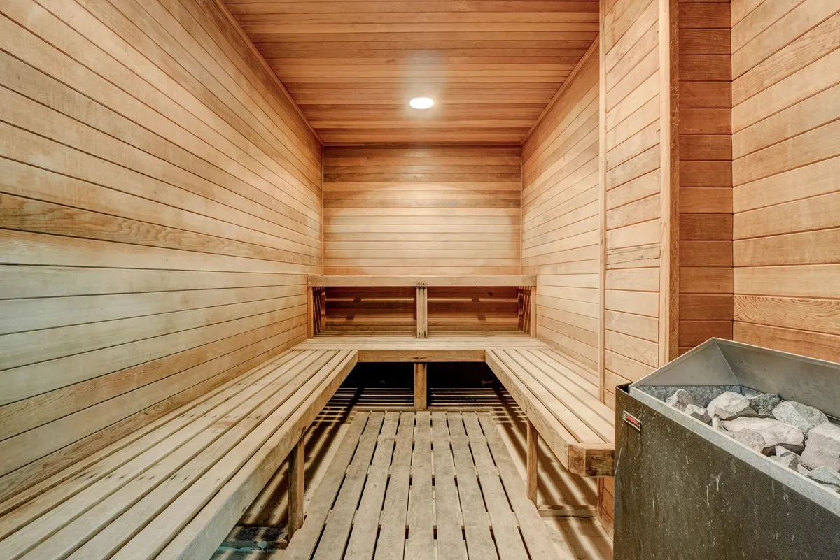 A serene interior of the sauna featuring smooth wooden benches and a stone heater. The tranquil setting invites guests to unwind and enjoy moments of relaxation and wellness.