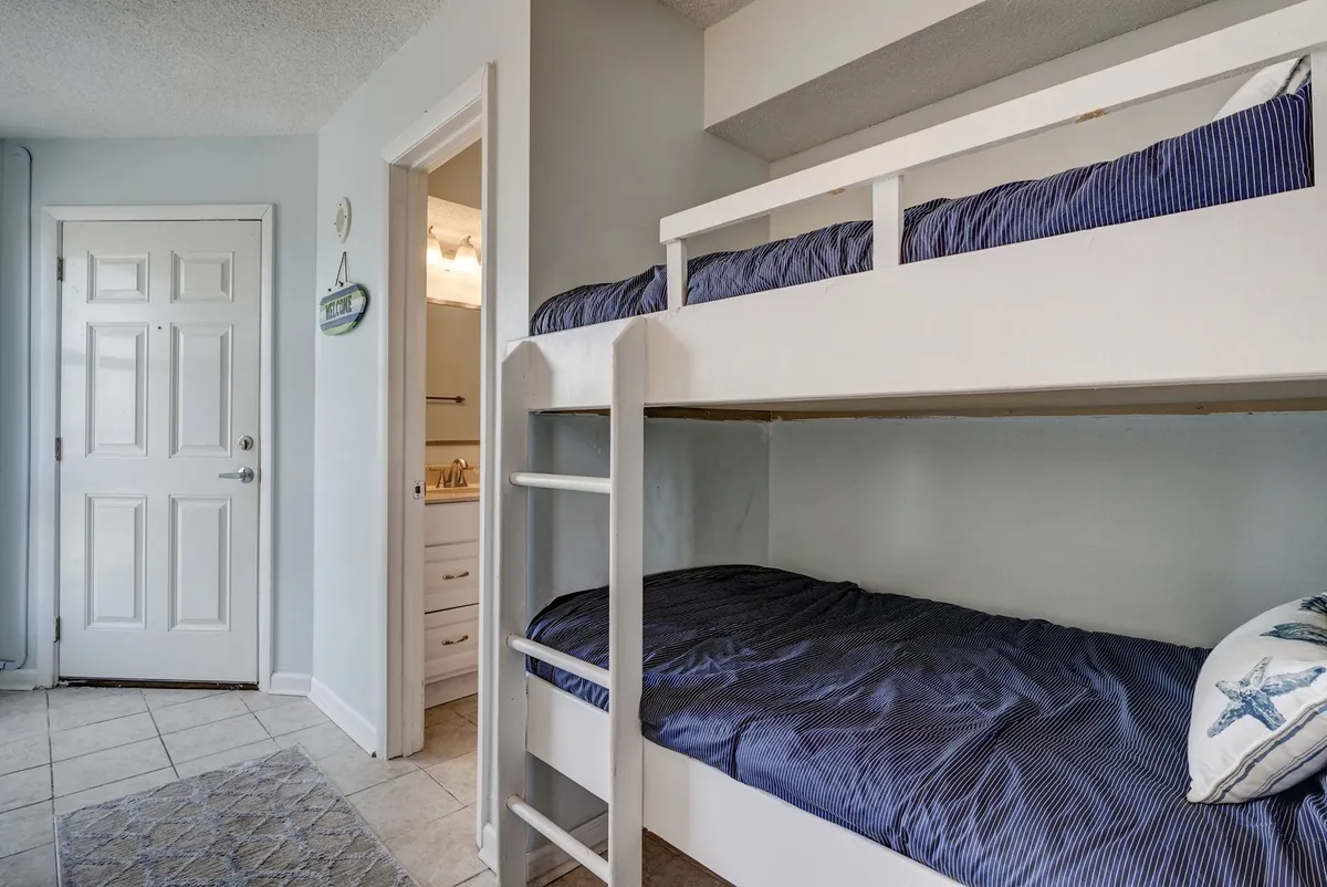 This image centers on a set of cozy bunk beds tucked into an alcove just off a hallway, with a visible doorway and bathroom entrance nearby. The space is inviting and thoughtfully designed for children, with soft lighting and playful bedding details.