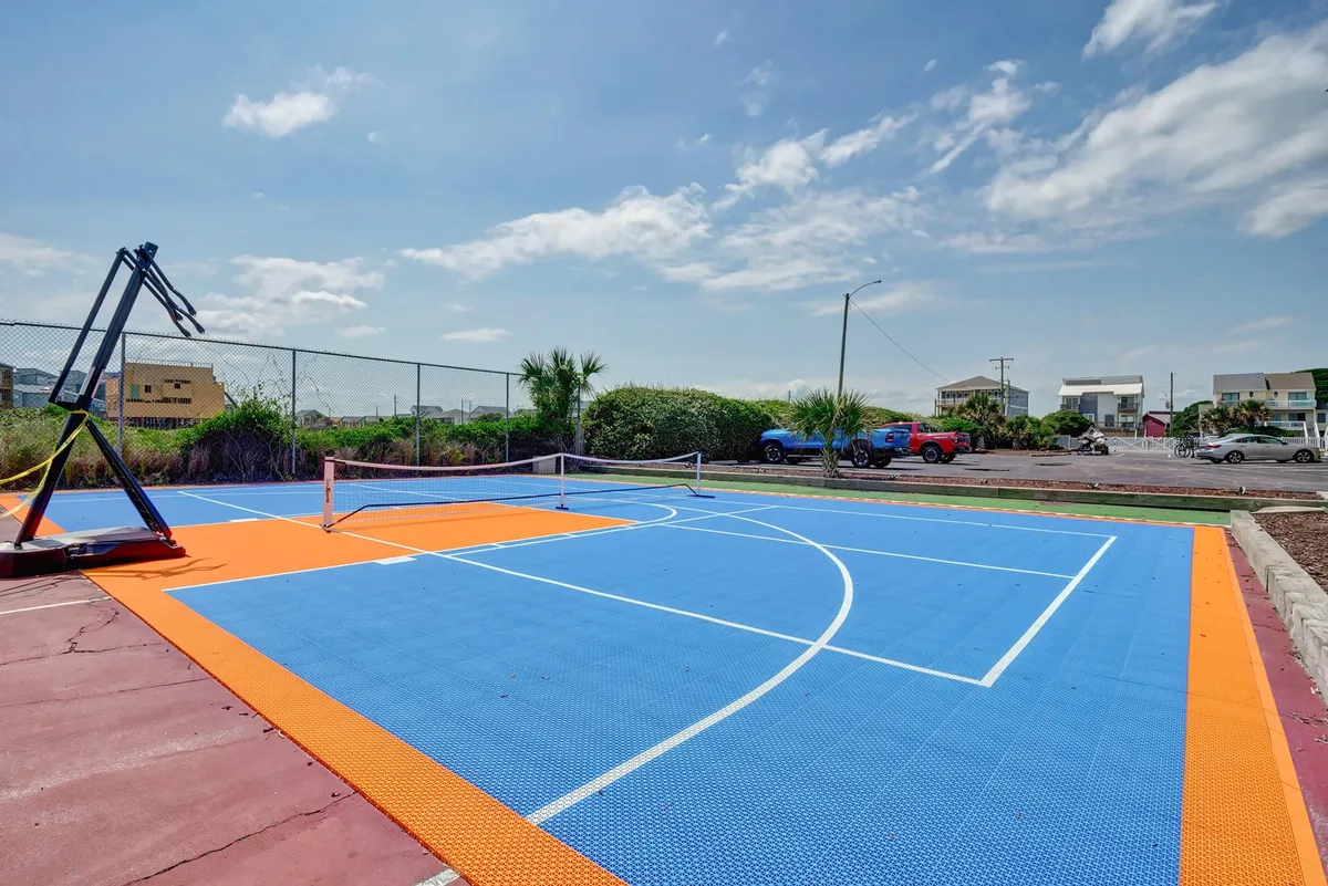 A vibrant exterior sports court featuring a basketball hoop and tennis net, surrounded by open space for a variety of outdoor activities. The area is well-maintained and set against a backdrop of clear skies, creating an inviting and active environment.