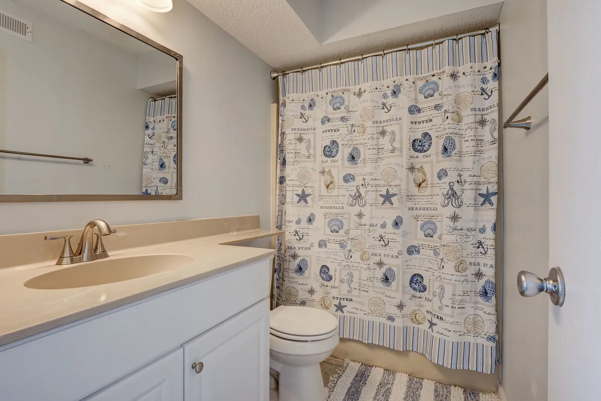A bathroom scene with a vanity and sink, shower curtain, and a well-lit mirror. The clean, fresh ambiance suggests a space designed for both morning routines and evening relaxation after a day in the sun.