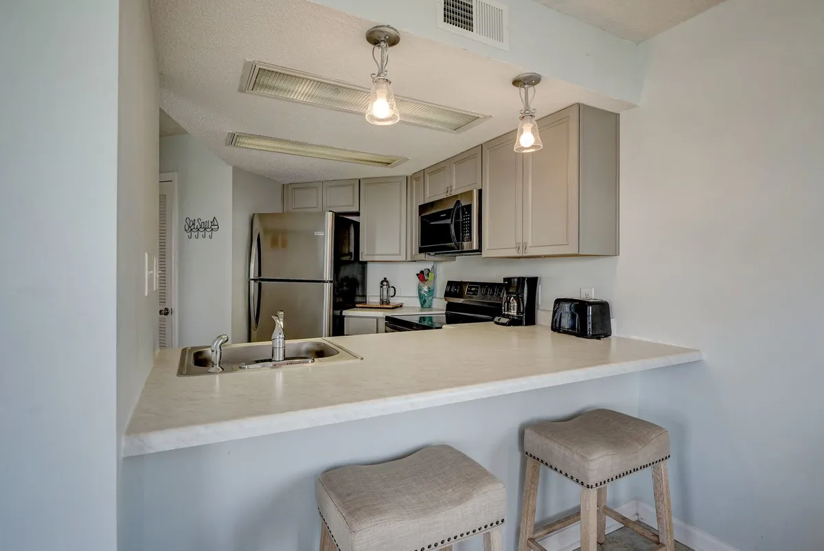 A welcoming, modern kitchen featuring a spacious island with bar stools, gleaming stainless steel appliances, and warm lighting. The open layout is perfect for preparing meals while chatting with guests or family, and the space feels both functional and inviting.