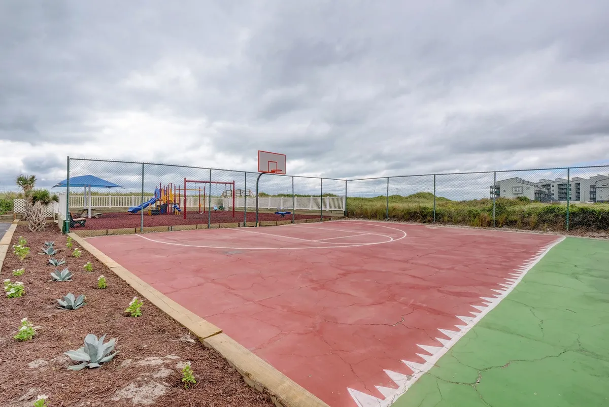 A dynamic exterior scene featuring a basketball court and a playground surrounded by landscaped gardens. Children are at play on the playground equipment, while others enjoy a friendly basketball game, capturing a family-friendly, energetic atmosphere.